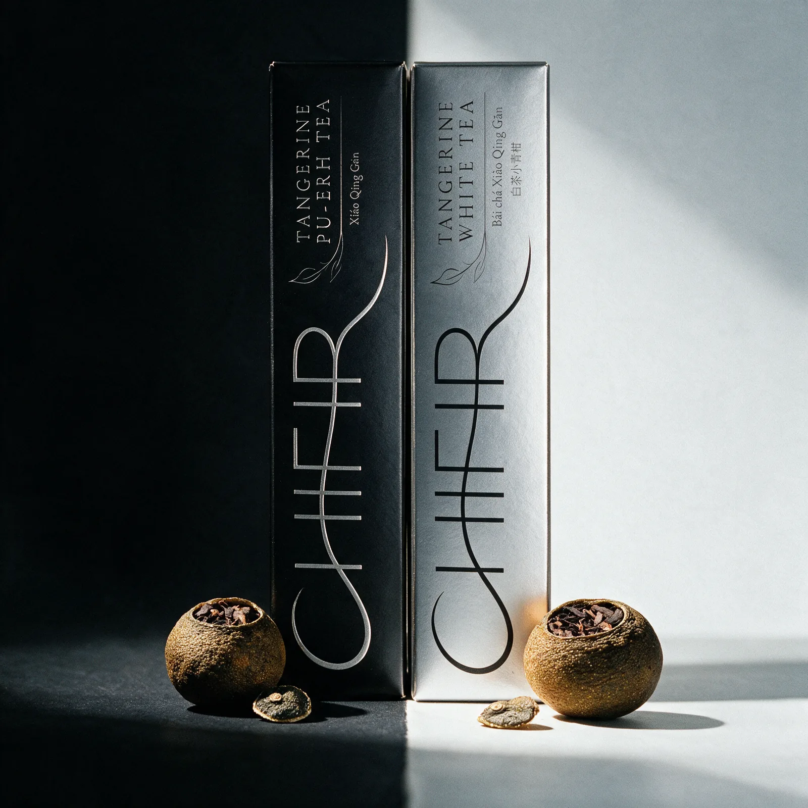 The black Tangerine Pu-erh carton standing in shadow beside the silver Tangerine White carton in daylight, one dried tangerine piece with its cut cap at the foot of each.